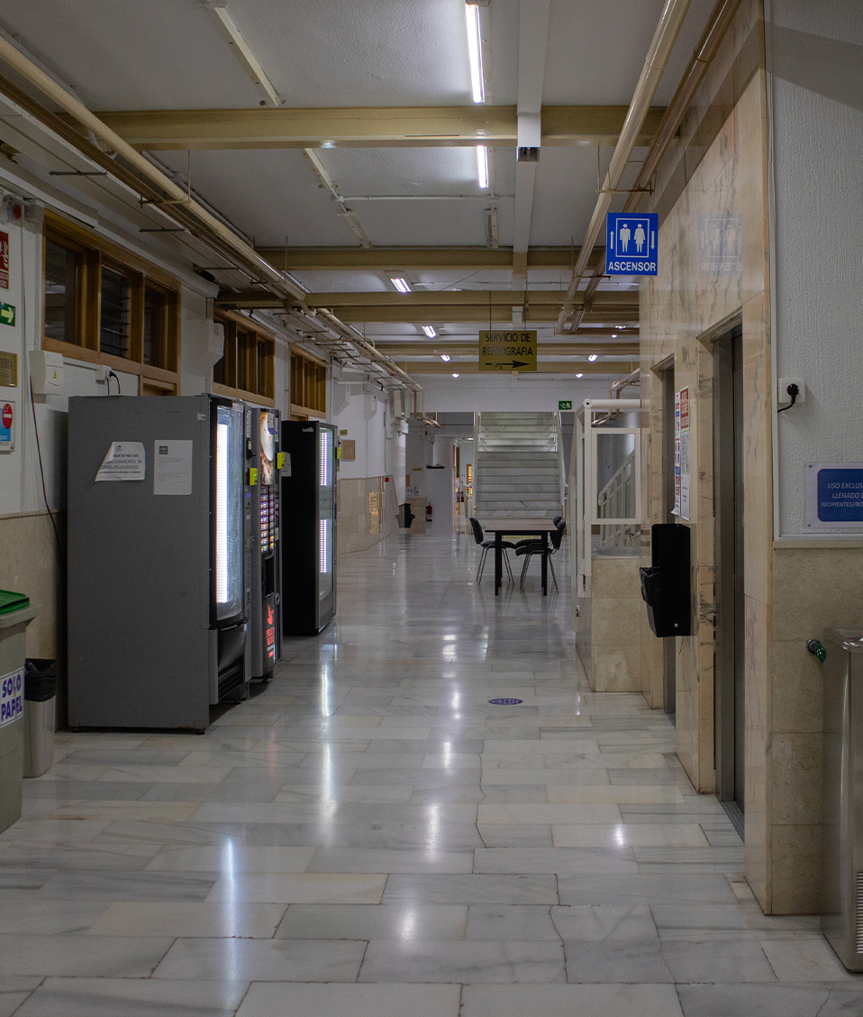 Pasillo del interior de la Facultad de psicología, con máquinas expendedoras, fuente y una mesa